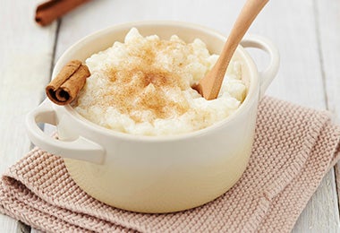 Una porción de arroz con leche, lychees y canela con una cuchara de madera.