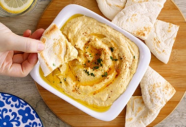 Recipiente lleno de hummus con pan pita, para acompañar la hamburguesa falafel.