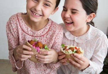 Niñas degustando alegremente pitas rellenas de falafel, un pan árabe muy similar a la focaccia italiana