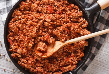 Salsa a la boloñesa con carne molida sobre una sartén y con una cuchara de madera