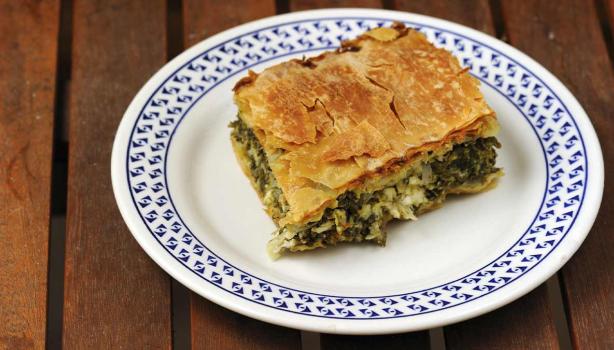 Una porción de la receta griega spanakopita sobre un plato blanco y azul.